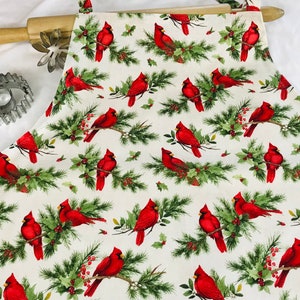 May include: White fabric apron with a repeating pattern of red cardinals perched on green pine branches with red berries.