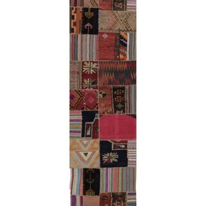 May include: A long, rectangular patchwork rug with a variety of geometric and abstract patterns. The rug features a mix of colors, including red, pink, blue, and beige. The design is made up of numerous rectangular patches sewn together.