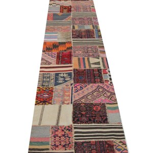 May include: A long, rectangular patchwork rug with a variety of patterns and colors. The rug is made up of numerous rectangular and square pieces of fabric, each with a unique design. Colors include red, blue, orange, and cream.