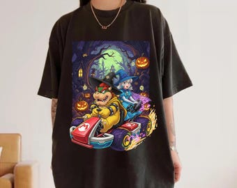 Może przedstawiać: Czarny t-shirt z kolorową grafiką Bowsera i Księżniczki Peach w gokarcie, w tematyce Halloween. Projekt zawiera dynie, przerażające tło lasu i płomienie. Gokart ma literę "M".