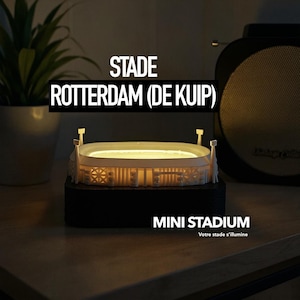 Op de afbeelding: Een miniatuur stadionmodel met de tekst "STADE ROTTERDAM (DE KUIP)" en "MINI STADIUM". Het model is van binnenuit verlicht en toont de architectonische details van het stadion. De basis is zwart en het stadion is wit.