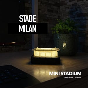 Könnte beinhalten: Ein Miniatur-Stadionmodell mit beleuchtetem Innenraum, auf einem schwarzen Sockel. Der Text "STADE MILAN" ist über dem Stadion und "MINI STADIUM" darunter zu sehen. Im Hintergrund ein Blumentopf.