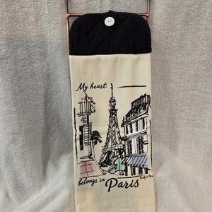 May include: A cream-colored kitchen towel with a black quilted top and a copper-colored metal hanger. The towel features a black and white illustration of the Eiffel Tower and Parisian buildings, with the text "My heart belongs in Paris."