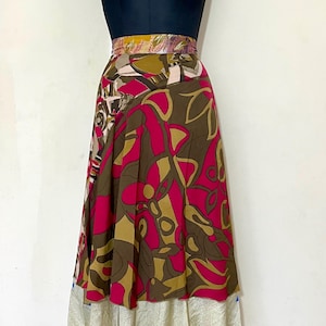 Könnte beinhalten: Ein farbenfroher Wickelrock mit einem lebendigen Blumenmuster in Rosa-, Braun- und Goldtönen. Der Rock hat ein mehrschichtiges Design mit einer cremefarbenen Unterlage. Der Bund ist mit einer Mischung aus Farben gemustert.