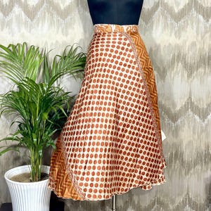 Peut inclure: Une jupe portefeuille avec un motif à pois marron et blanc sur le panneau avant, et des panneaux latéraux présentant un imprimé chevron géométrique marron et beige. La jupe est présentée sur un buste de mannequin noir, montrant une coupe évasée.