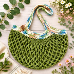 May include: A crescent-shaped crochet tote bag featuring a solid olive green mesh body and a wide, multicolored strap with hues of blue, white, and peach. A small brown rectangular tag is attached to the upper edge of the bag.