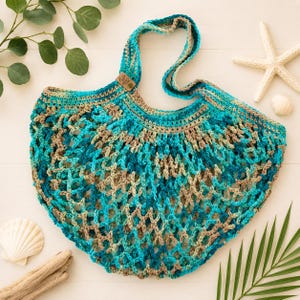 May include: A crochet market bag featuring an open mesh design in variegated shades of turquoise, teal, and tan. The bag has a single shoulder strap and a small rectangular brown leather-like tag attached to the upper edge near the strap base.
