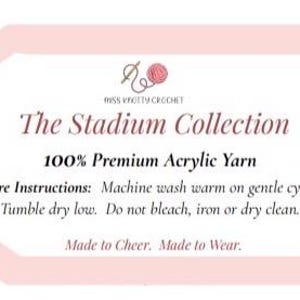 May include: A light pink tag with the text "MISS KNOTTY CROCHET" and "The Stadium Collection". The tag also states "100% Premium Acrylic Yarn" and care instructions. The tag has a light pink border and a small illustration of a ball of yarn.