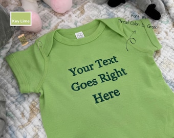 May include: A key lime green baby onesie with the text "Your Text Goes Right Here" embroidered in dark green. The onesie has short sleeves and a round neckline. The thread color is dark green, and the font is number 4.