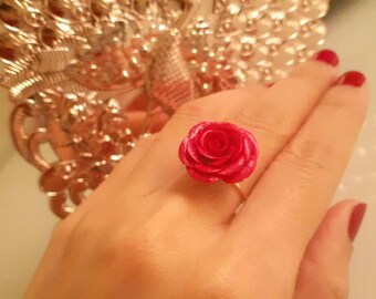 May include: A red rose ring with a gold band. The rose is the focal point, with detailed petals. The ring is a piece of jewelry, likely for fashion or special occasions.