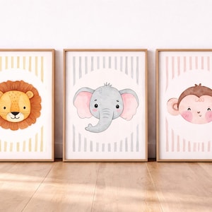 May include: Three framed watercolor prints featuring adorable animal faces: a lion, an elephant, and a monkey. Each print has a light-colored background with vertical stripes and a circular design behind the animal's face. The frames are a light brown color.