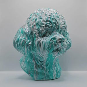 May include: A decorative dog head sculpture with a unique marbled effect. The sculpture features a mix of teal, white, and grey colours, creating a swirling pattern across the surface. The dog's features, including the eyes, nose, and fur, are clearly defined.
