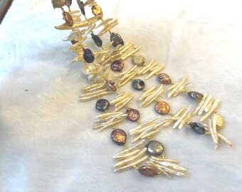 May include: A layered necklace featuring a combination of off-white, brown, and gold-toned beads. The necklace has a cascading design with various shapes and sizes of beads, creating a textured and elegant look. The beads are strung together with gold-colored metal.