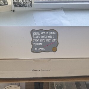 May include: A white Cricut Maker machine with a sticker that reads "Wanted: someone to hand-feed me Cheetos while I crochet so my fingers don't get orange. No weirdos." The sticker has a gray border and a pink crochet hook.