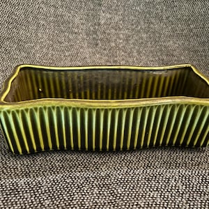 May include: A rectangular ceramic planter with a ribbed exterior. The planter is a dark olive green colour with a slightly scalloped rim. The interior is a darker shade of green.