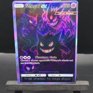 May include: A holographic Gengar ex Pok&eacute;mon trading card. The card features a purple and black illustration of Gengar and other Pok&eacute;mon characters. Text on the card includes "Gengar ex", "Phantom Gate", and "from shadow to mega abyss".