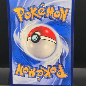 May include: A blue Pok&eacute;mon trading card featuring the Pok&eacute;mon logo in yellow and a Pok&eacute; Ball design. The card has a white and red Pok&eacute; Ball in the center, surrounded by a swirling blue background.