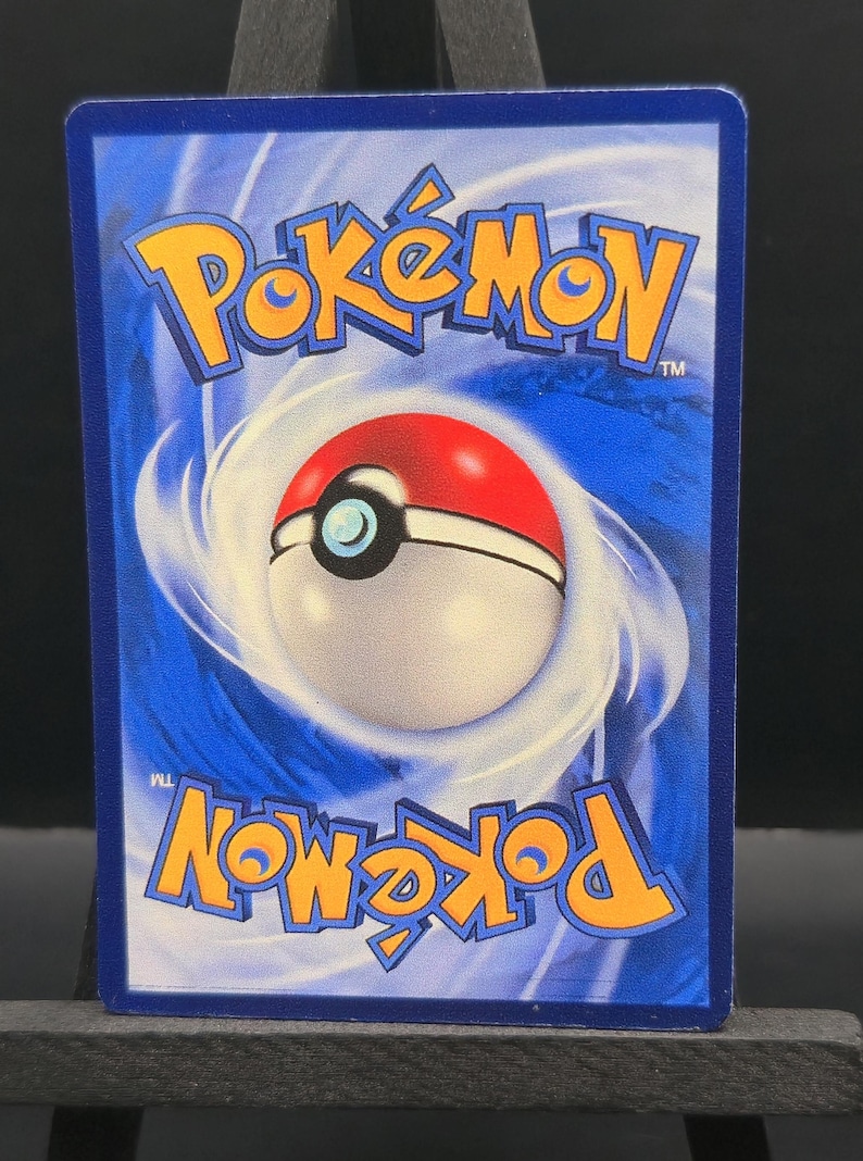 May include: A blue Pok&eacute;mon trading card featuring the Pok&eacute;mon logo in yellow and a Pok&eacute; Ball design. The card has a white and red Pok&eacute; Ball in the center, surrounded by a swirling blue background.