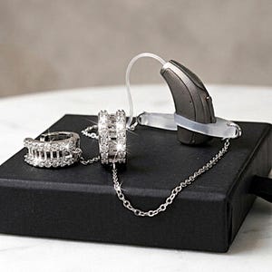 Ett par örhängen med kedja för hörapparater. Rodiumpläterade smycken för cochleaimplantat.