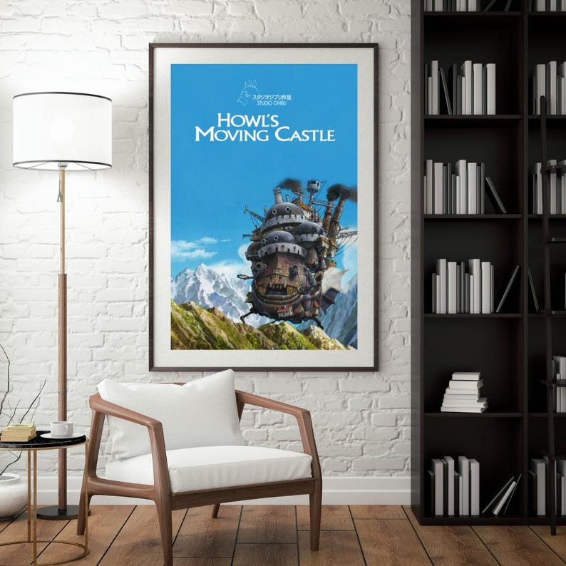 May include: Framed poster featuring the animated film "Howl's Moving Castle." The artwork depicts the castle with a blue sky background and mountain range. The poster has a dark brown frame and is displayed on a white brick wall.