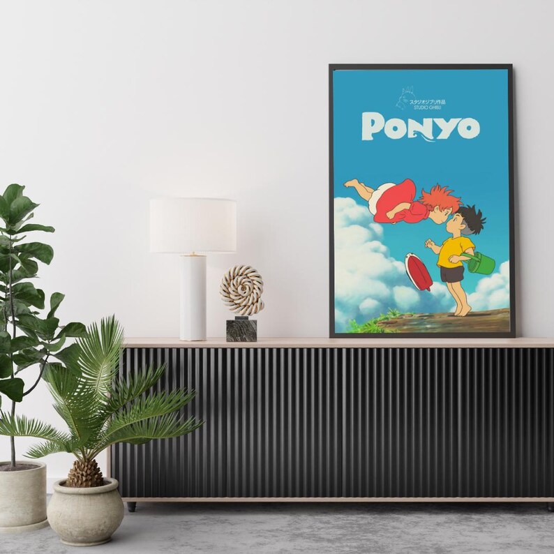 May include: Framed art print of the animated film "Ponyo." The image shows two cartoon characters kissing, set against a blue sky with clouds. The title "Ponyo" is in large white letters. The print is in a black frame.