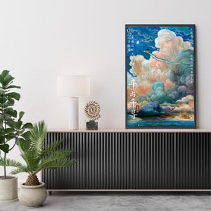 Op de afbeelding: Een ingelijste poster met een fantasierijke sc&egrave;ne van een draak in een bewolkte lucht, met Japanse tekst en data. Het kunstwerk wordt getoond op een zwarte kast, met een witte lamp en decoratieve objecten. De kleuren van de poster zijn levendig.