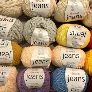 May include: A selection of colourful yarn balls in various shades, such as yellow, blue, orange, and purple. Each ball is labelled with the word "jeans" and the brand "YarnArt". The yarn is suitable for knitting or crochet projects.