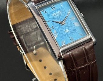 Reloj de pulsera vintage Seiko Slim de cuarzo con tanque: esfera con números romanos y correa de piel.