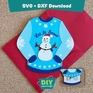May include: A light blue papercraft sweater with a snowman design and the text "Let It Snow." The sweater is on a red envelope. A smaller version of the sweater is also present. The image includes the text "SVG + DXF Download" and "DIY papercrafts."