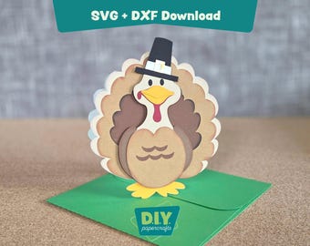 May include: A layered papercraft turkey wearing a pilgrim hat, set on a green envelope. The turkey has a brown body, beige feathers, and a yellow beak. The text "SVG + DXF Download" is at the top.