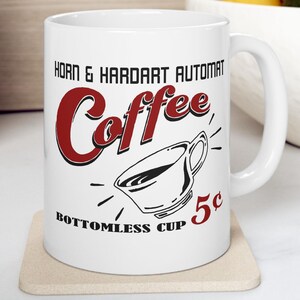 May include: White ceramic coffee mug with the words "Horn & Hardart Automat Coffee" in black and red lettering. A graphic of a coffee cup is below the word "Coffee", and the text "Bottomless Cup 5¢" is at the bottom.
