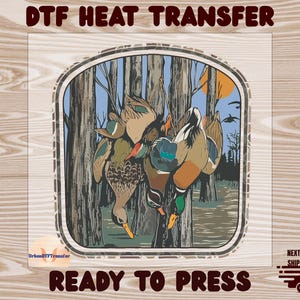 May include: DTF heat transfer design featuring a hunting scene with ducks hanging from trees. The image has a rustic, outdoorsy theme, with text that reads "READY TO PRESS". The design includes a forest backdrop and a setting sun.