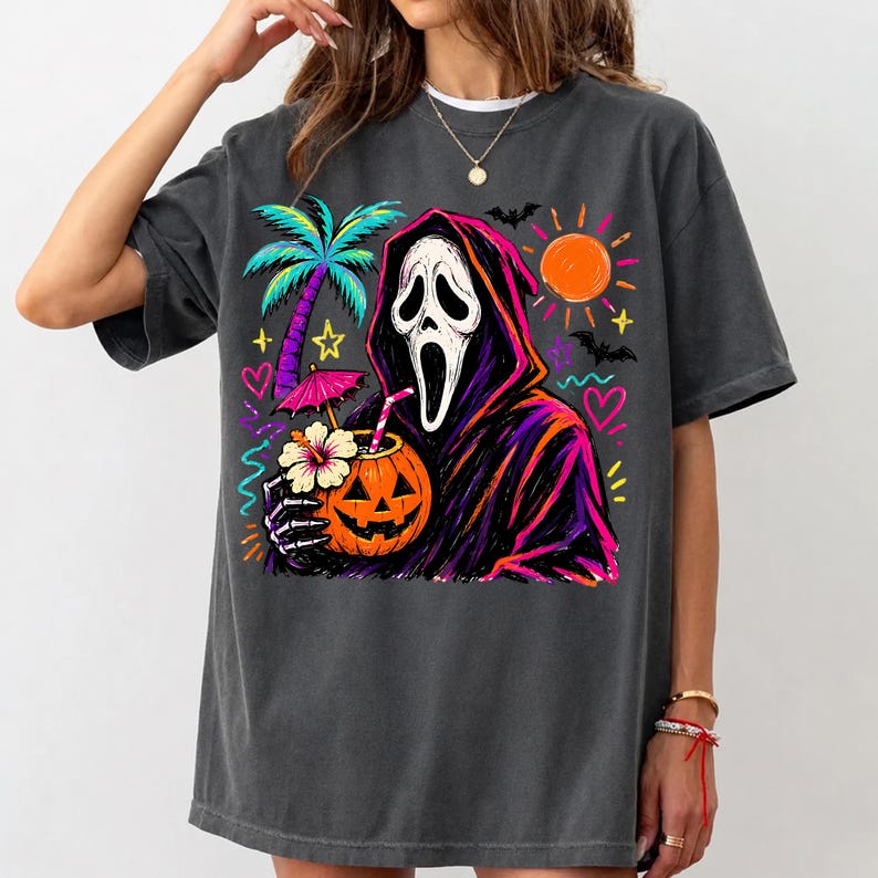 Pode incluir: Uma t-shirt cinzento-carv&atilde;o com uma estampa gr&aacute;fica de uma figura encapuzada com m&aacute;scara branca segurando uma bebida numa ab&oacute;bora com palhinha e uma flor de hibisco. O design inclui uma palmeira, um sol, morcegos, cora&ccedil;&otilde;es e estrelas em cores n&eacute;on.