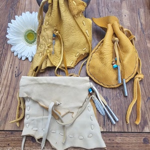 May include: Three leather pouches with fringe and beads. The pouches are made of light brown and white leather.