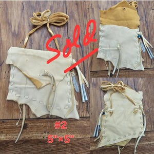 May include: A white leather pouch with fringe and a beaded strap. The pouch is 5 inches by 5 inches and is labeled #2. The pouch is sold.