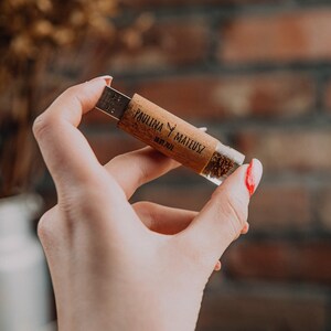 May include: A clear USB drive with a wooden casing, filled with small, dark particles. The casing is inscribed with the names "PAULINA Y MATEUSZ" and a date. The USB drive is held against a blurred background of a brick wall.