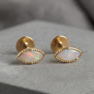 May include: A pair of stud earrings featuring marquise-shaped opals set in gold metal with a beaded edge. Each earring has a post back and displays a milky white stone with iridescent flashes of color, showcasing a refined and classic design.