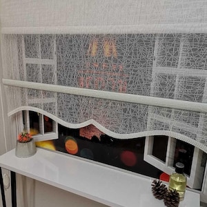 Peut inclure: Rideaux de fenêtre blancs et transparents avec un motif délicat en forme de toile d'araignée. Les rideaux sont superposés à une fenêtre avec vue sur les lumières de la ville. Une étagère blanche contient une petite plante en pot, une bouteille et des pommes de pin.