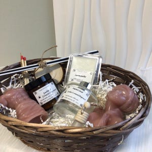 May include: A wicker basket containing scented products, including a candle, wax melts, and a diffuser. The products are labeled with the text "Leather & Oriental Fragrance". The items are in shades of pink and brown. The basket is on a white surface.