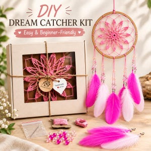 May include: A DIY dream catcher kit featuring a cardboard box with a window displaying a pink crocheted web. Beside it hangs a finished dream catcher with a wooden hoop, pink web, and dangling pink and light pink feathers with clear beads.