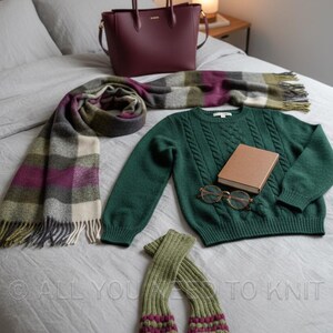 May include: An assortment of autumn and winter accessories, including a burgundy tote bag, a green cable-knit jumper, a plaid scarf with fringe, a small book, glasses, and green and purple arm warmers. The items are arranged on a bed.