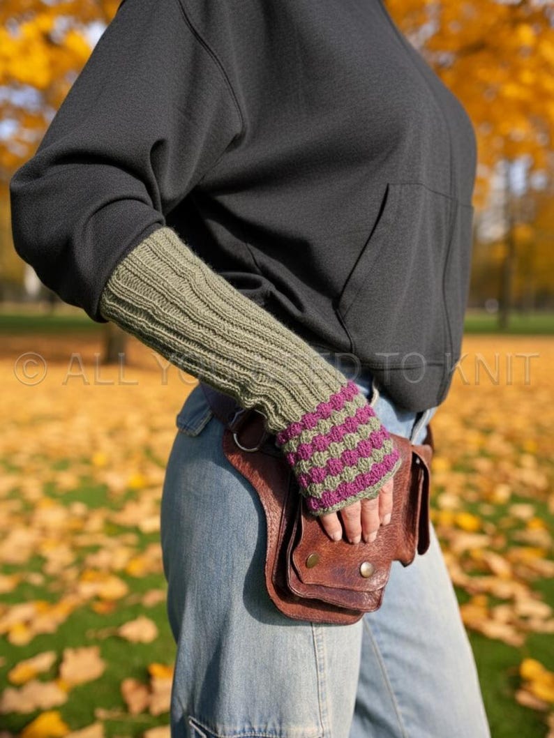 May include: Olive green and purple striped fingerless gloves. The gloves are worn with a black hoodie and blue jeans. A brown leather fanny pack is also visible. The text "ALL YOU NEED TO KNIT" is in the image.
