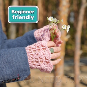 May include: A pair of light pink crochet fingerless gloves featuring an openwork shell pattern. The gloves are worn with a blue blazer and a green stone ring. A rectangular sign with a white border displays the text Beginner friendly.