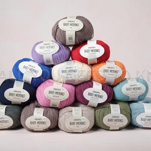 May include: A pyramid of colorful yarn balls labeled "Baby Merino." The yarn balls are in various colors, including blue, purple, red, orange, pink, and green. Each ball has a white label with black text.