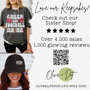 K&ouml;nnte beinhalten: Dunkelgraues T-Shirt mit "CHEER AND FOOTBALL MAMA" Grafik. Eine schwarze Kappe mit "MOM EST. 2025" ist ebenfalls abgebildet. Das Bild enth&auml;lt Text: "Love our Keepsakes?" und "Check out our Sister Shop!"