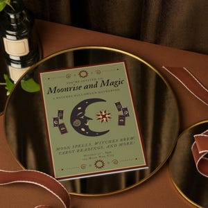 Puede incluir: Una tarjeta de invitación de Halloween con el texto "Moonrise and Magic" y una ilustración de media luna. La tarjeta está sobre un espejo con borde dorado, con una cinta marrón y una botella verde oscuro en el fondo.