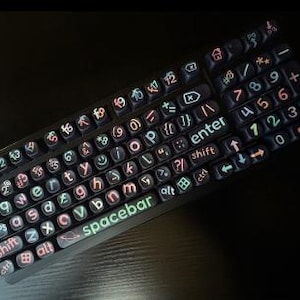 May include: A black keyboard with illuminated keys. The keys display letters, numbers, and symbols in various colors, including green, orange, and white. The spacebar is lit up in green. The keyboard is angled on a dark surface.
