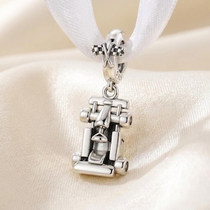 Peut inclure: Un charm en argent en forme de voiture de course de Formule 1, avec un cockpit et des roues détaillés. La bélière est gravée S925 et présente un motif de drapeau à damier. Le charm est suspendu à un ruban blanc, avec une finition métallique polie.