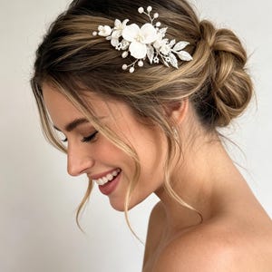 May include: A hair comb featuring white floral elements, small pearl-like beads, and silver-toned metallic leaves. The decorative piece is arranged in a cluster with delicate wire branches extending outward, creating a botanical-inspired hair accessory.