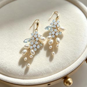 May include: A pair of gold-tone drop earrings featuring clusters of small, pale blue round stones, marquise-cut light blue crystals, and white oval pearls. The components are arranged in a branch-like design suspended from gold-tone ear hooks.